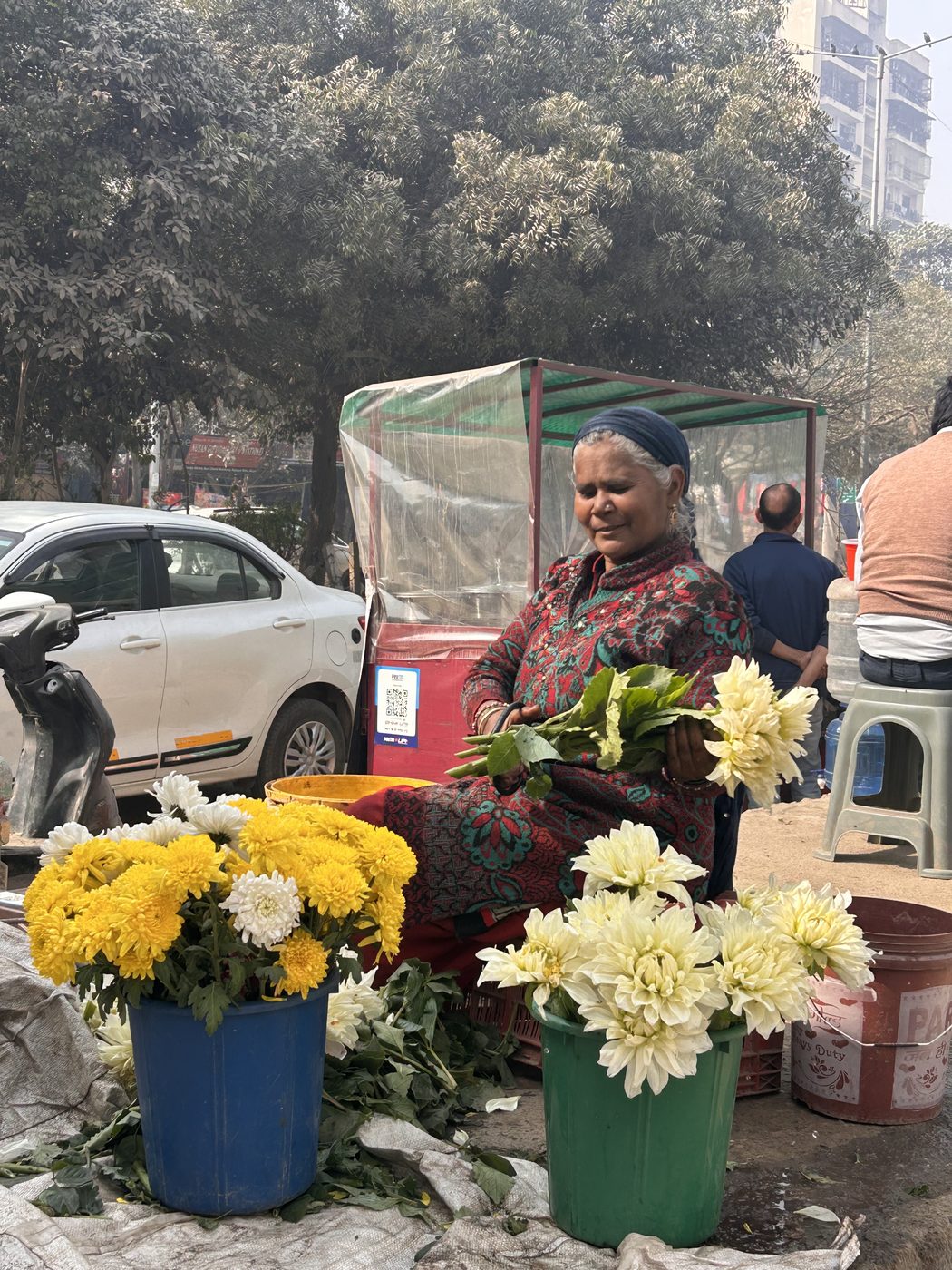 A flower seller at a roadside stall, buckets of marigolds and chrysanthemums